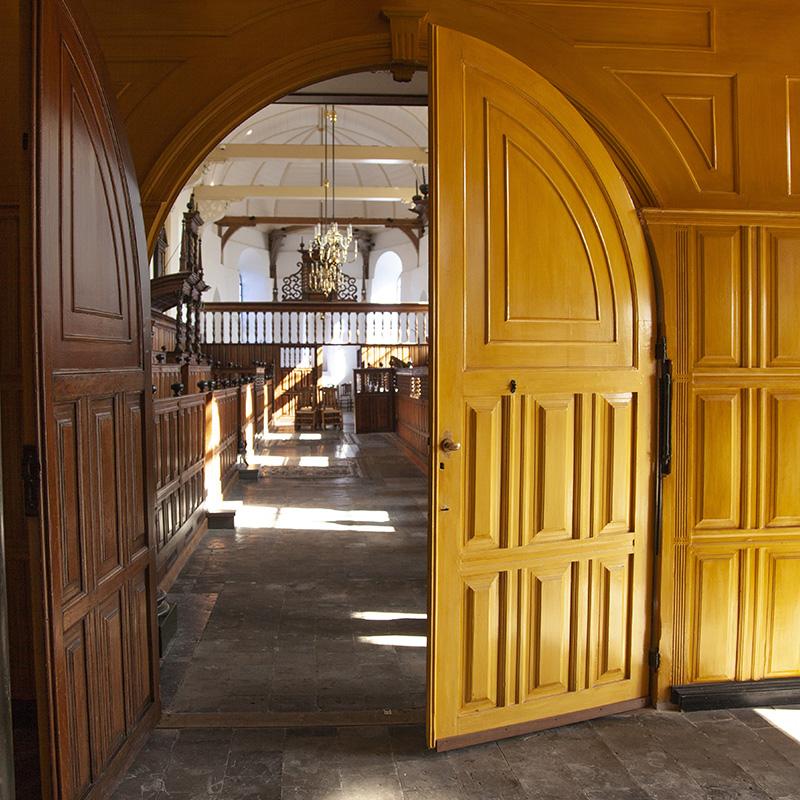 Achter grote halfopen staande deuren is het kerkinterieur van de Laurentiuskerk te zien.