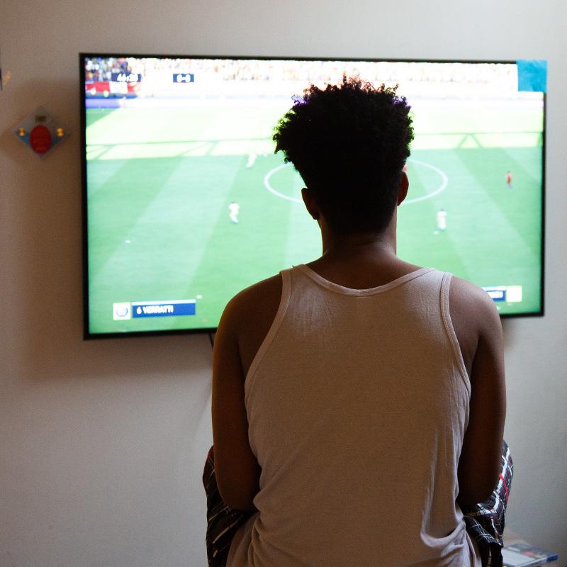 Een jonge alleenstaande vluchteling kijkt een voetbalwedstrijd.
